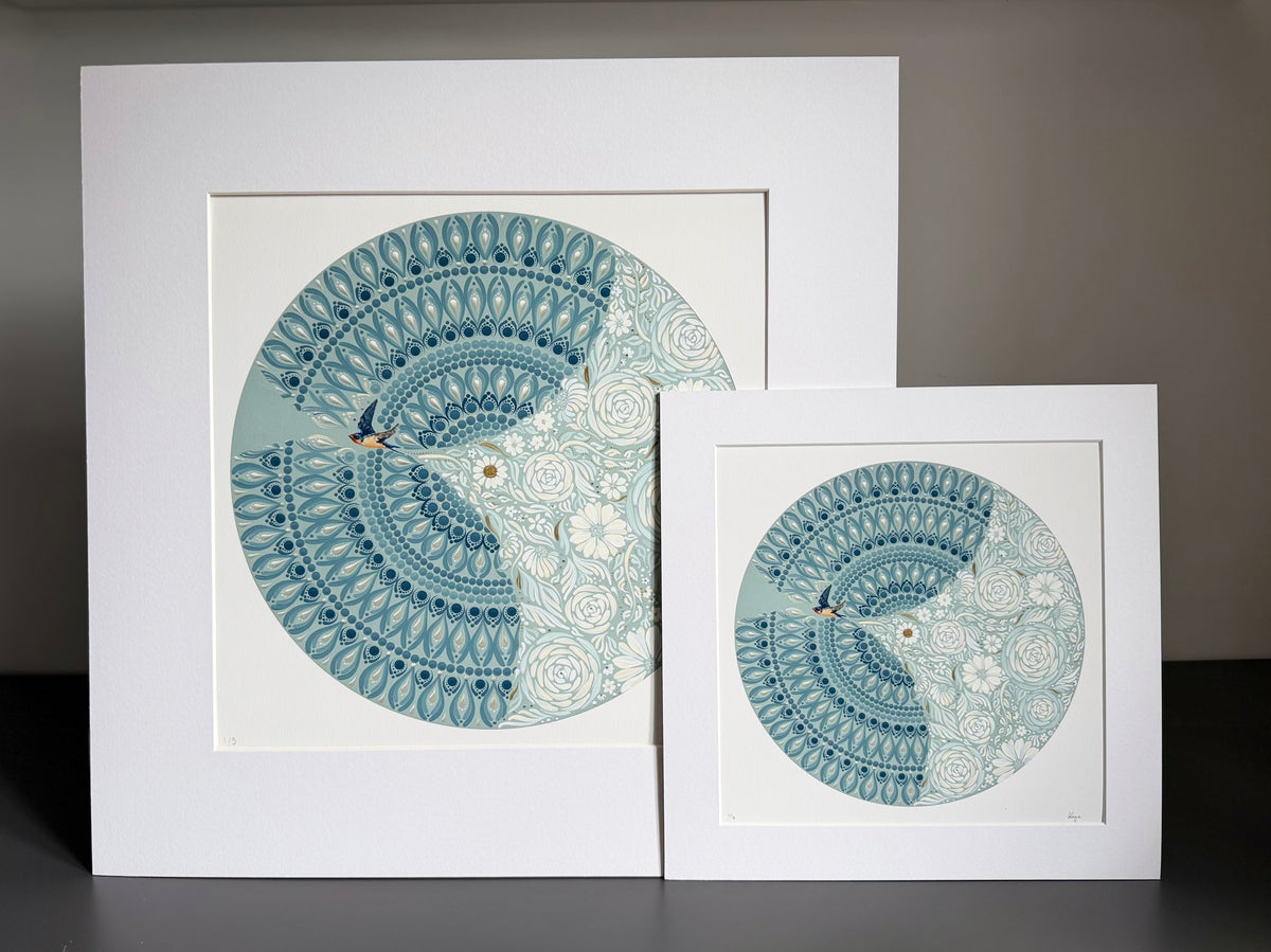 Two mounted  art prints with white mats, featuring a circular mandala-style illustration in shades of teal, blue, and white, displayed against a neutral gray background.